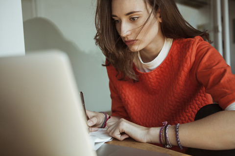 Junge Frau arbeitet an Laptop und Papieren, lizenzfreies Stockfoto