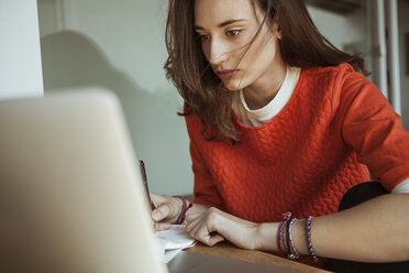 Junge Frau arbeitet an Laptop und Papieren - FEXF00297