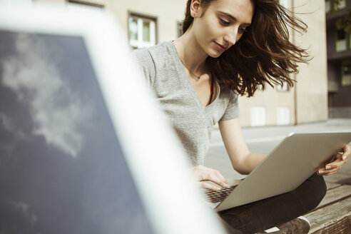 Young woman sitting on bench using laptop - FEXF00305