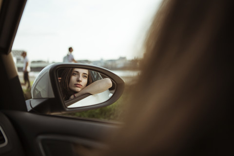 Spiegelbild einer jungen Frau im Auto, die aus dem Fenster schaut, lizenzfreies Stockfoto