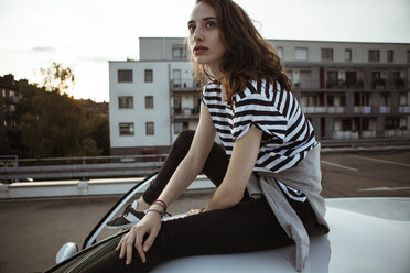 Serious young woman sitting on car roof - FEXF00313