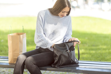 Young woman sitting on bench looking in bag - MMAF00171