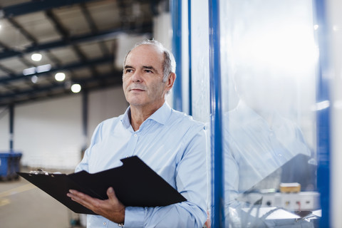 Älterer Geschäftsmann steht in der Werkstatt und hält Akten, lizenzfreies Stockfoto