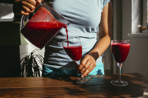 Woman pouring fresh squeezed juice into glasses, partial view - MOMF00282