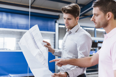 Zwei Geschäftsleute stehen in einer Werkstatt und besprechen Pläne, lizenzfreies Stockfoto