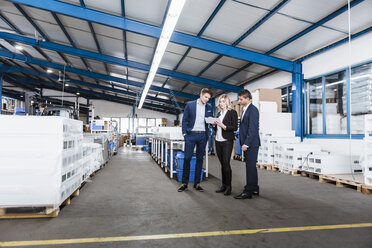 Three business people discussing on shop floor, using digital tablet - DIGF03057