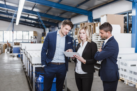 Drei Geschäftsleute diskutieren in der Werkstatt mit einem digitalen Tablet, lizenzfreies Stockfoto