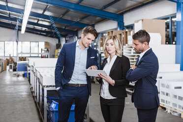 Three business people discussing on shop floor, using digital tablet - DIGF03058