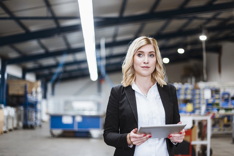 Blond businesswoman standing in shop floor, using digital tablet stock photo