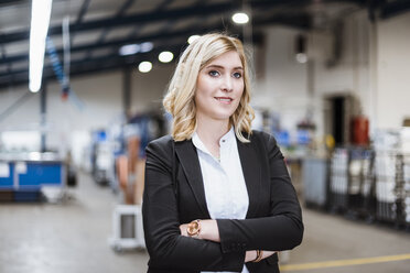 Blonde businesswoman standing on shop floor with arms crossed, portrait - DIGF03067