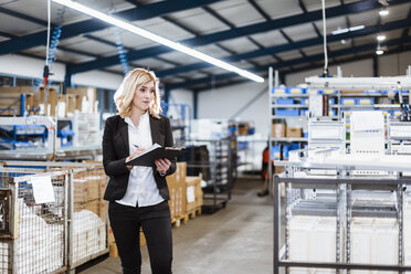 Blond businesswoman standing in shop floor, writing in notebook - DIGF03068