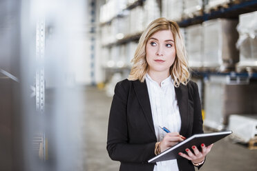 Blond businesswoman standing in storehouse, writing in notebook - DIGF03073