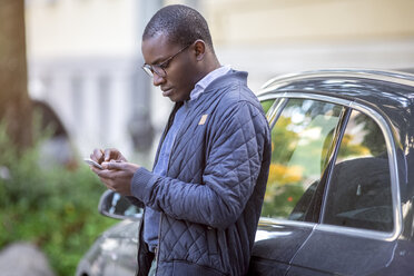 Young man leaning against car using cell phone - MMAF00185