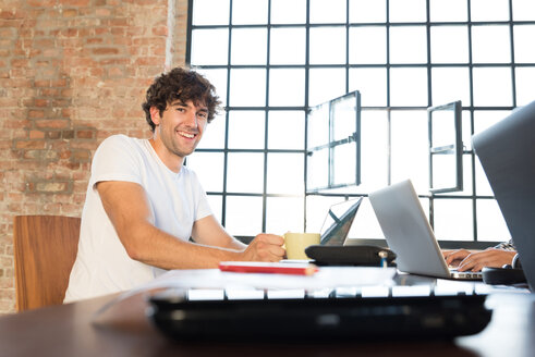 Glücklicher Jungunternehmer bei der Arbeit im Co-Working Space, mit Laptop - SPCF00179