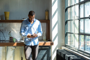 Young entrepreneur standing in company kitchen, drinking coffee, using smartphone - SPCF00208