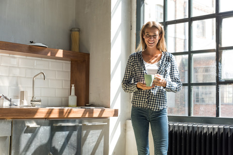Junge Unternehmerin steht in der Firmenküche und trinkt Kaffee, lizenzfreies Stockfoto