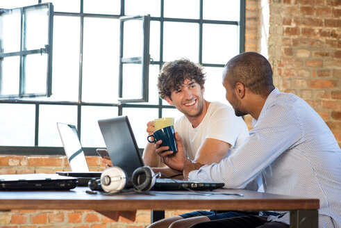 Zwei junge Geschäftsleute arbeiten zusammen in einem Co-Working Space und benutzen Laptops - SPCF00245