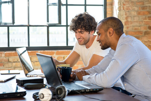 Zwei junge Geschäftsleute arbeiten zusammen in einem Co-Working Space und benutzen Laptops - SPCF00246