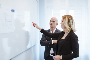 Businessman looking at businesswoman at whiteboard in office - DIGF03083