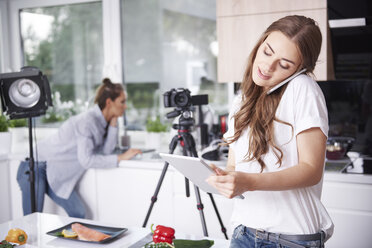 Woman using cell phone and tablet in kitchen - ABIF00038