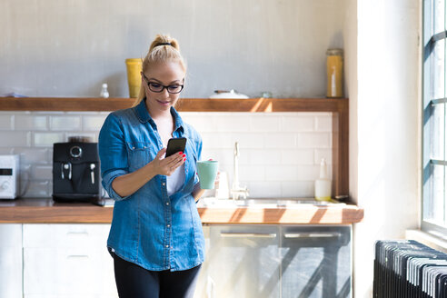 Geschäftsfrau steht mit Kaffeetasse in der Küche und schaut auf ein Tablet - SPCF00251
