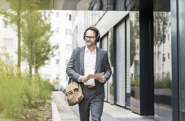 Portrait of smiling businessman with documents and headphones - UUF12080
