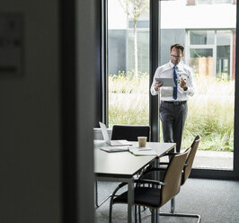 Businessman with atomic model and tablet in his office - UUF12089