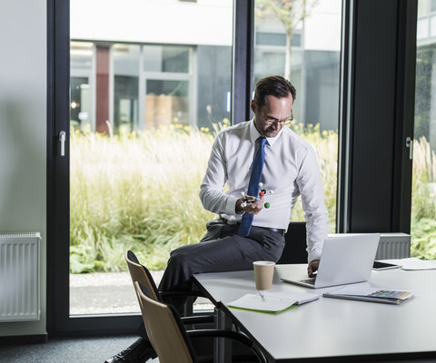 Geschäftsmann mit Atommodell und Laptop in seinem Büro, lizenzfreies Stockfoto