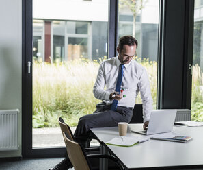 Businessman with atomic model using laptop in his office - UUF12091