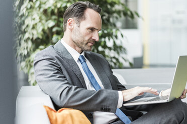 Geschäftsmann sitzt in der Lobby und benutzt einen Laptop - UUF12095