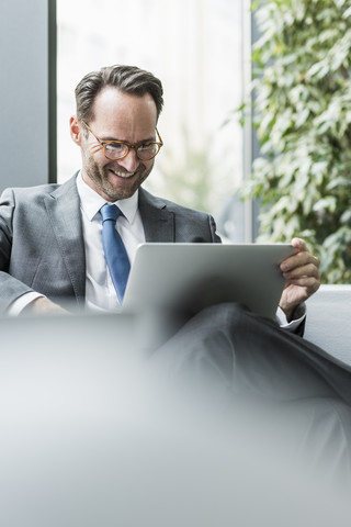 Geschäftsmann sitzt in der Lobby und benutzt einen Laptop, lizenzfreies Stockfoto