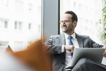 Businessman sitting in lobby using laptop - UUF12097