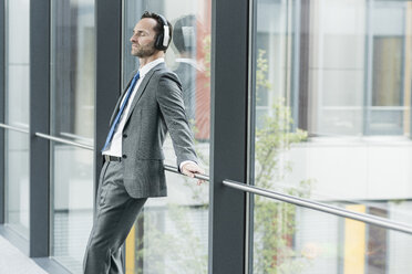 Portrait of businessman with eyes closed listening music with headphones - UUF12100