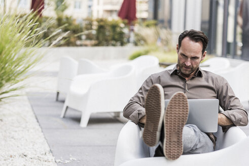 Geschäftsmann sitzt auf einer Terrasse und benutzt einen Laptop - UUF12110