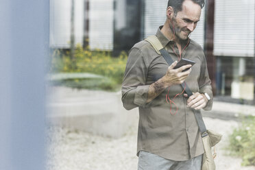 Portrait of smiling businessman using smartphone and earphones - UUF12114