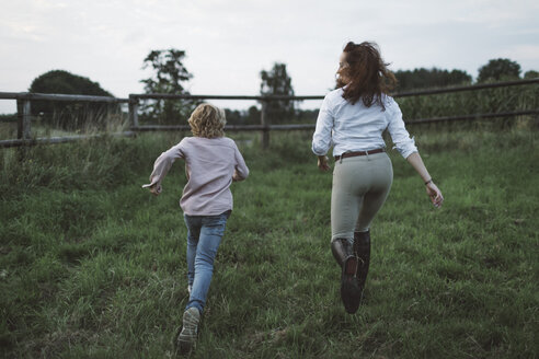 Rückenansicht eines Jungen und einer jungen Frau, die Seite an Seite auf einer Koppel laufen - KMKF00041