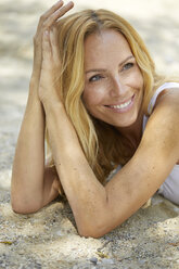 Portrait of happy strawberry blonde woman lying on the beach - PNEF00221