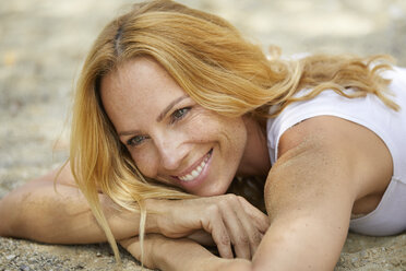 Portrait of happy strawberry blonde woman lying on the beach - PNEF00222