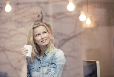Porträt einer lächelnden blonden Frau mit Kaffeetasse, die aus dem Fenster schaut - PNEF00231