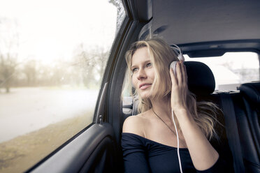 Porträt einer jungen Frau, die im Auto sitzt und mit Kopfhörern Musik hört - PNEF00236