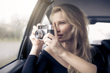 Woman sitting in car taking picture with camera - PNEF00237