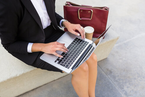 Geschäftsfrau mit modischer Ledertasche und Kaffee zum Mitnehmen auf einer Bank sitzend und mit Laptop, Teilansicht - MGIF00185