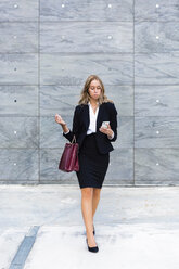 Businesswoman with fashionable leatherbag looking at cell phone - MGIF00199