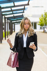 Geschäftsfrau mit modischer Ledertasche schaut auf ihr Handy - MGIF00200