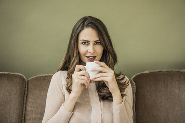 Porträt einer Frau, die auf der Couch sitzt und eine Tasse Kaffee trinkt - MOEF00184