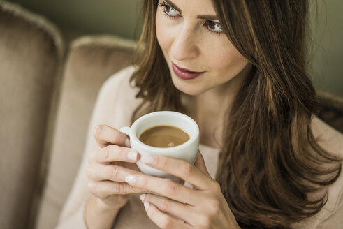 Porträt einer Frau, die auf einer Couch sitzt und eine Tasse weißen Kaffee trinkt - MOEF00185