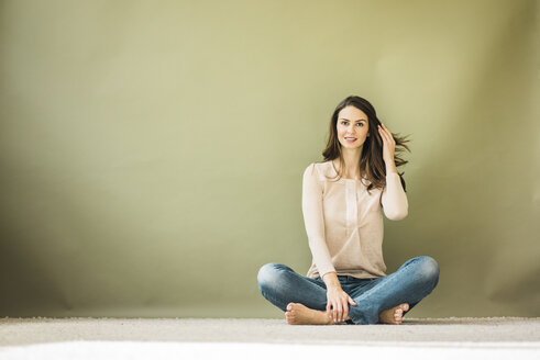 Porträt einer Frau, die vor einem grünen Hintergrund auf dem Boden sitzt - MOEF00191