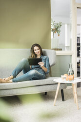 Young woman sitting on the couch using tablet - MOEF00194
