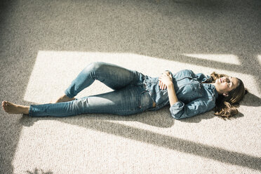 Junge Frau liegt auf dem Teppich im Wohnzimmer und genießt das Sonnenlicht - MOEF00197