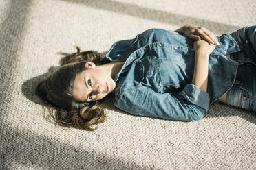 Porträt einer jungen Frau, die auf einem Teppich im Wohnzimmer liegt und das Sonnenlicht genießt - MOEF00199